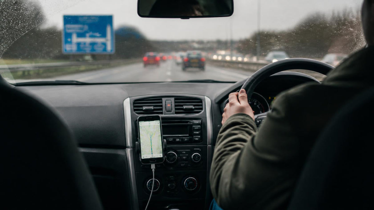 Driver on a rainy UK dual carriageway with a phone in an air vent holder showing the route